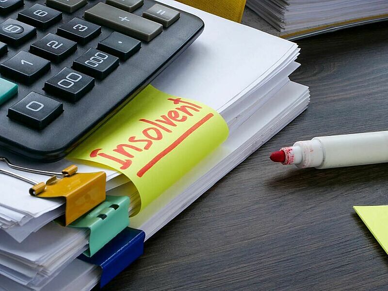 Taschenrechner auf einem Stapel Papieren mit dem Wort insolvent