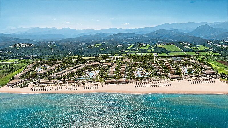 Hinter einem langen Sandstrand befinden sich viele Hotelgebäude, die an mehreren Pools liegen