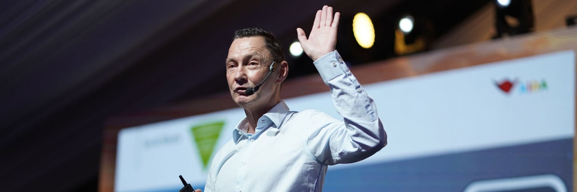 Bei einer Tagung steht ein Redner mit Headset auf der Bühne und richtet sich ans Publikum.