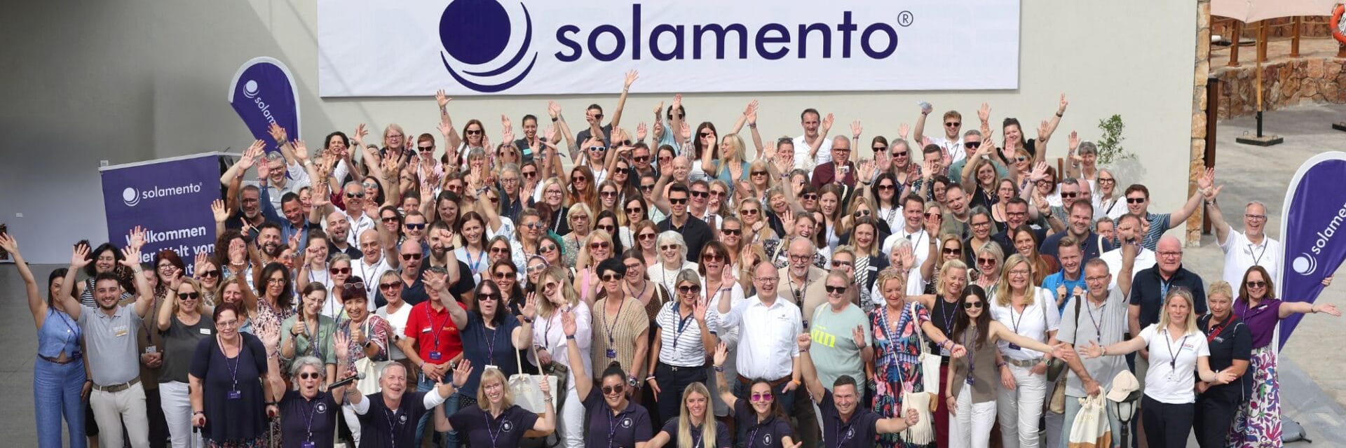 Gruppenfoto der Solamento-Jahrestagung 2024 im Aldiana Naga Bay in Hurghada: Über 140 Reiseberaterinnen und -reiseberater sowie rund 40 Partner und Leistungsträger stehen und jubeln gemeinsam vor einem großen Solamento-Logo auf der Hotelterrasse.