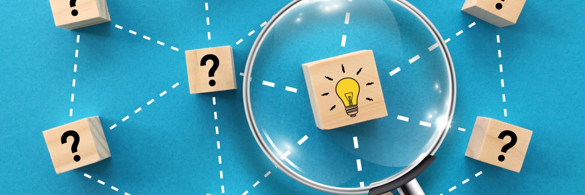 Holzklötze mit Fragezeichen sind durch gestrichelte Linien miteinander verbunden; eine Lupe vergrößert einen Klotz mit einer leuchtenden Glühbirne darauf – symbolisch für die Suche nach Lösungen oder Ideen.