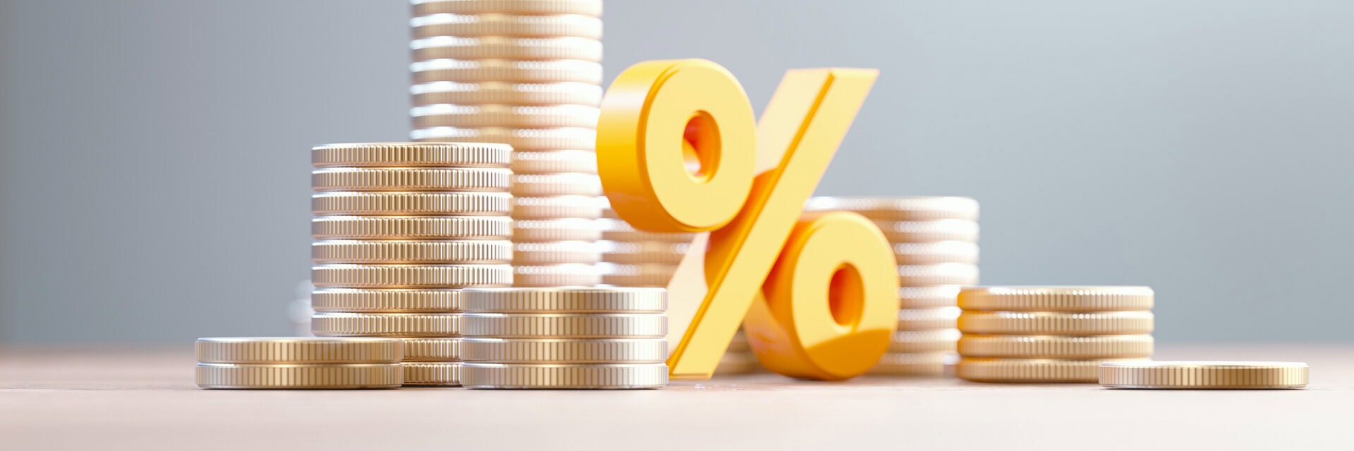 Mehrere gestapelte Münzen stehen auf einem Tisch, daneben befindet sich ein großes gelbes Prozentzeichen.