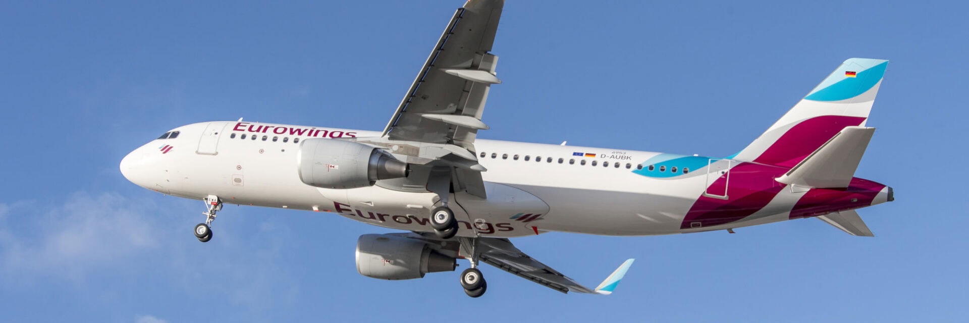 Ein Airbus A320 der Fluggesellschaft Eurowings ist im Landeanflug vor blauem Himmel zu sehen. Das Flugzeug trägt die charakteristischen Farben und das Logo von Eurowings. Die Aufnahme zeigt das Passagierflugzeug mit ausgefahrenem Fahrwerk.