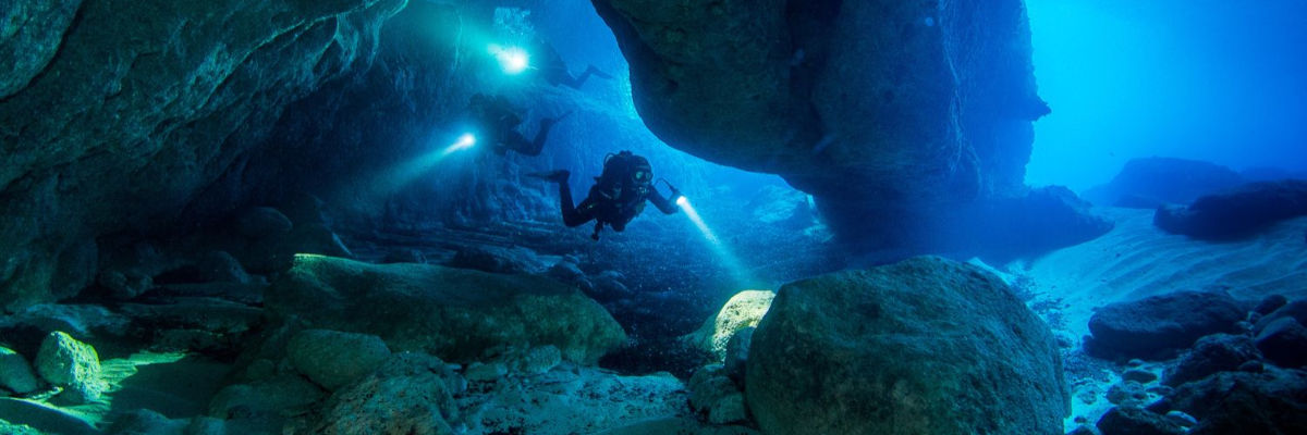 Zwei Taucher unter Wasser, die mit einem Licht ausgestattet durch eine unterirdische Höhle schwimmen.
