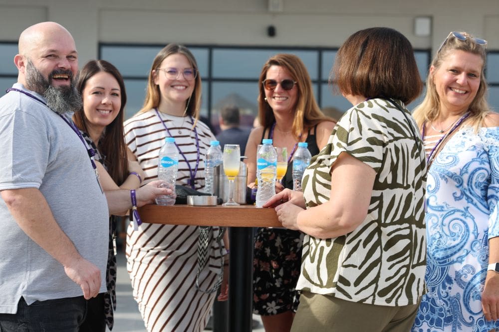 Eine Gruppe von Reiseberaterinnen steht um einen Stehtisch herum, sie lächeln in die Kamera.