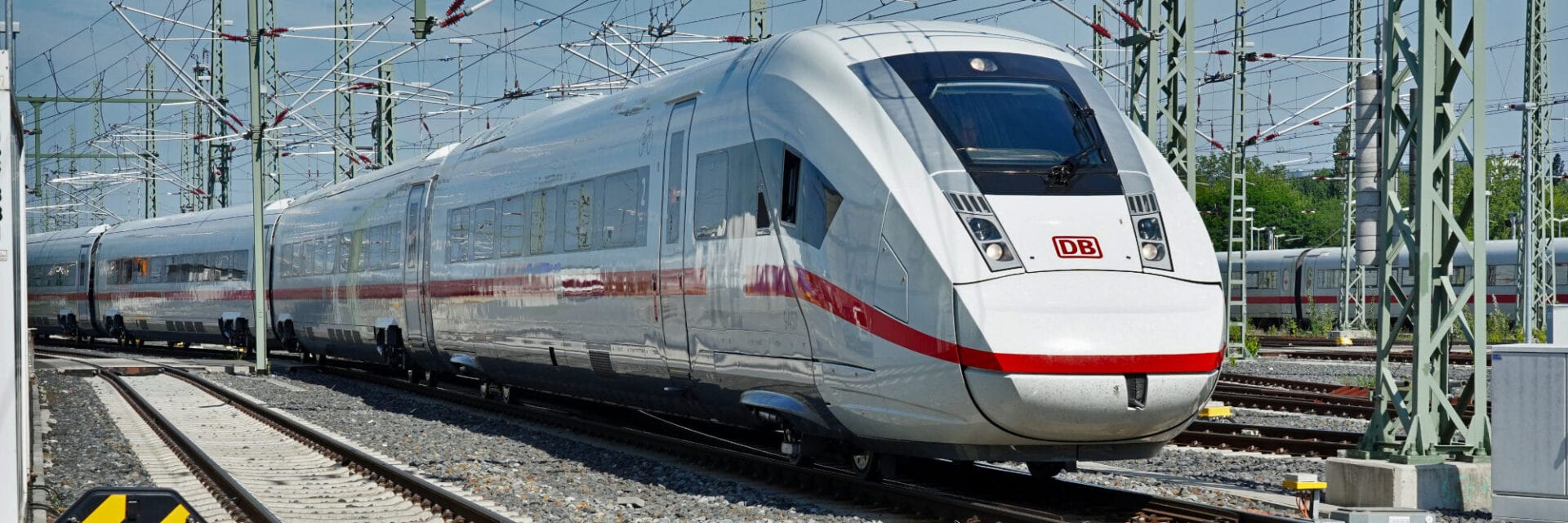 Das Foto zeigt einen modernen ICE der Deutschen Bahn, der auf einer elektrifizierten Bahnstrecke steht. Der Hochgeschwindigkeitszug ist von zahlreichen Oberleitungsmasten umgeben.