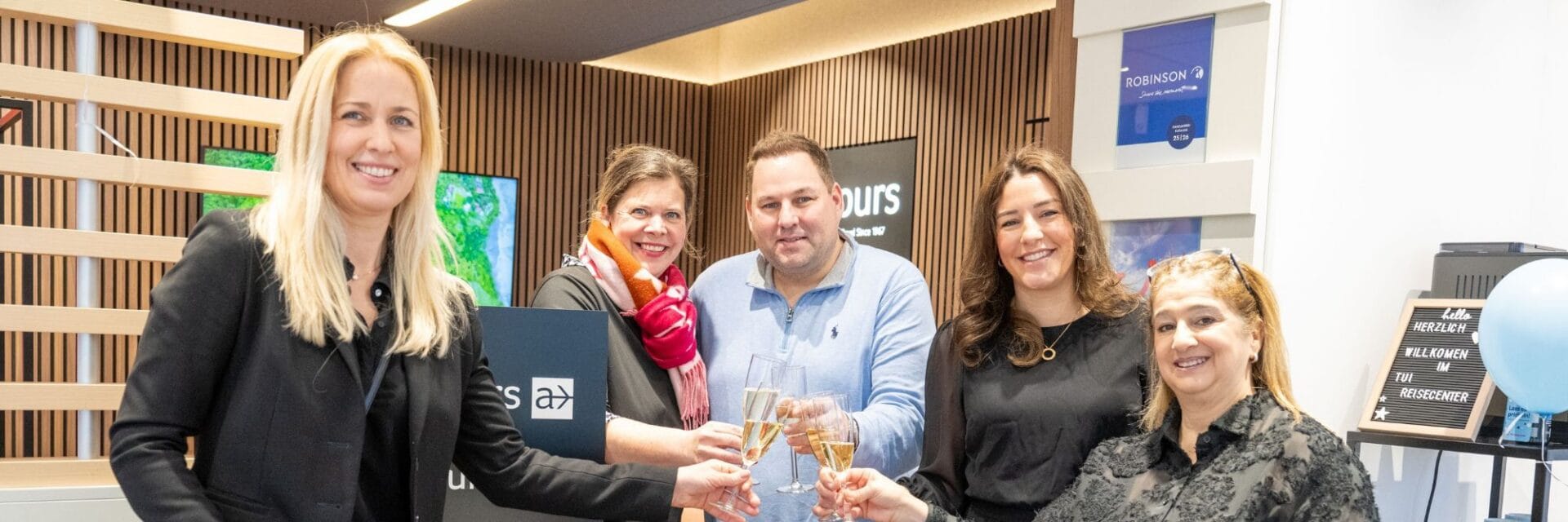 Mehrere Mitarbeitende stoßen mit Sektgläsern zur Eröffnung in einem modernen TUI Reisecenter an.