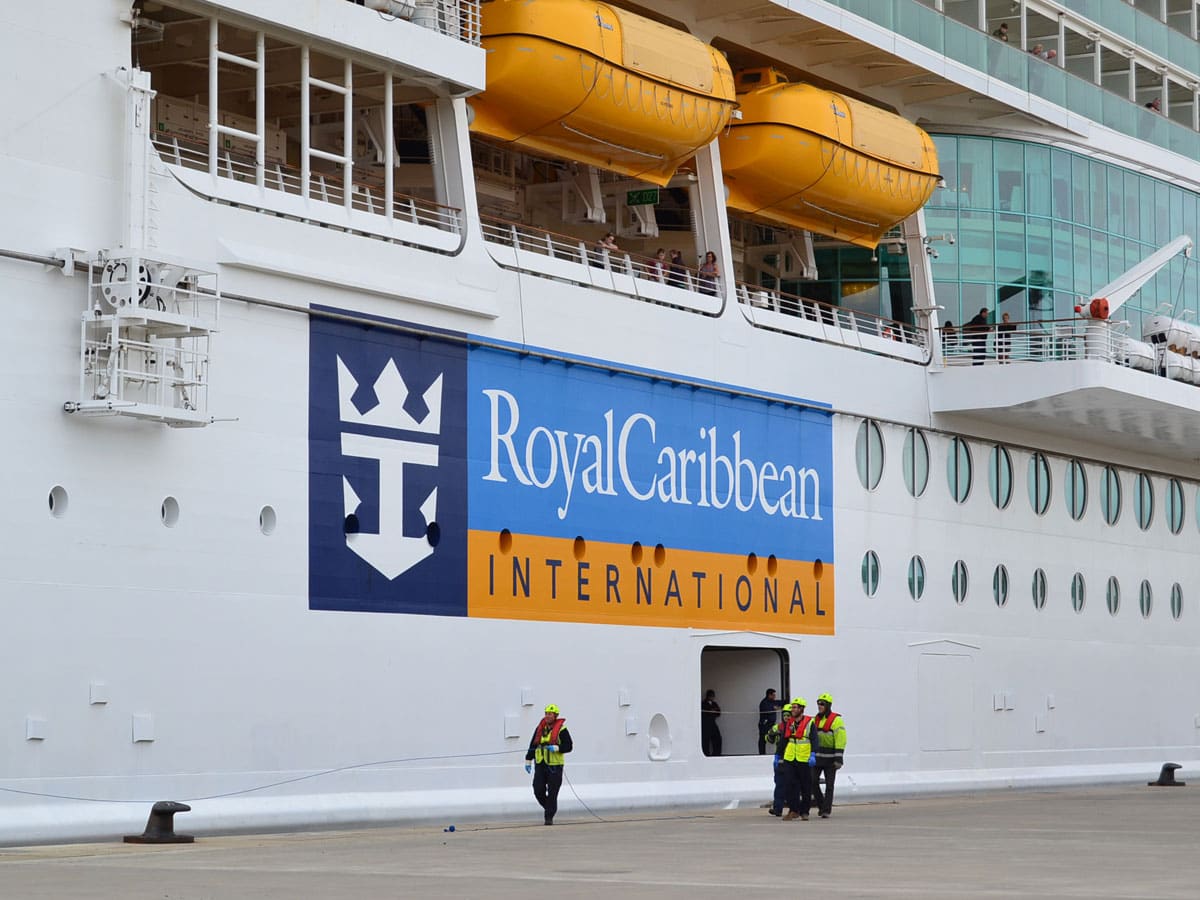 Teilansicht eines Kreuzfahrtschiffs an der Pier. Der Ausschnitt zeigt die Schiffswand mit dem Reedereischriftzug Royal Caribbean