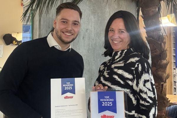 Ein Mann und eine Frau stehen in einem Reisebüro und halten jeweils eine Urkunde der Auszeichnung „Top Reisebüro 2025“ von Alltours in die Kamera.