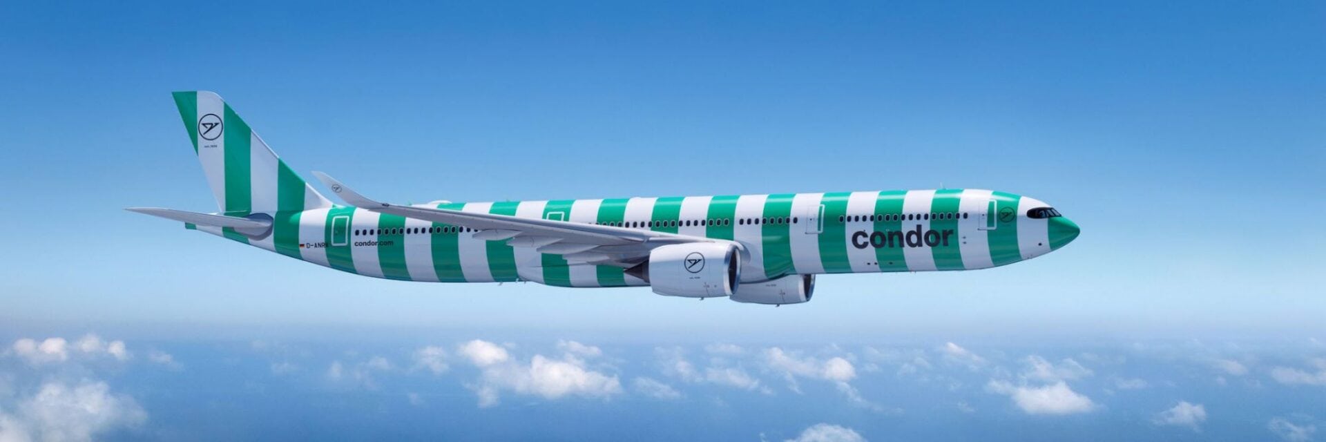 Passagierflugzeug der Airline Condor im grün‑weißen Streifendesign im Landeanflug über dem Meer unter blauem Himmel mit vereinzelten Wolken.