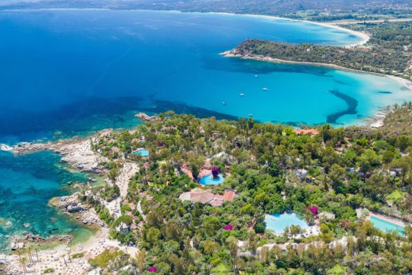 Auf einer grün eingewachsenen Halbinsel inmitten einem blauen Meer sind einige Hoteldächer zu sehen.