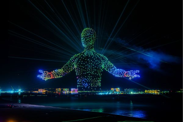 Nächtliche Drohnenshow über der Küste von Ras Al Khaimah: Tausende leuchtende Drohnen formen eine große Figur am Himmel, darunter sind Strand und Stadtlichter zu sehen.