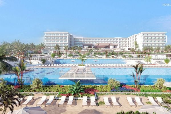 Das Bild zeigt das luxuriöse Riu Palace Hotel Swahili Beach mit mehreren großen Pools, umgeben von Palmen und zahlreichen Sonnenliegen unter strahlend blauem Himmel. Im Vordergrund sind die gepflegten Gartenanlagen und die großzügige Poollandschaft gut sichtbar.