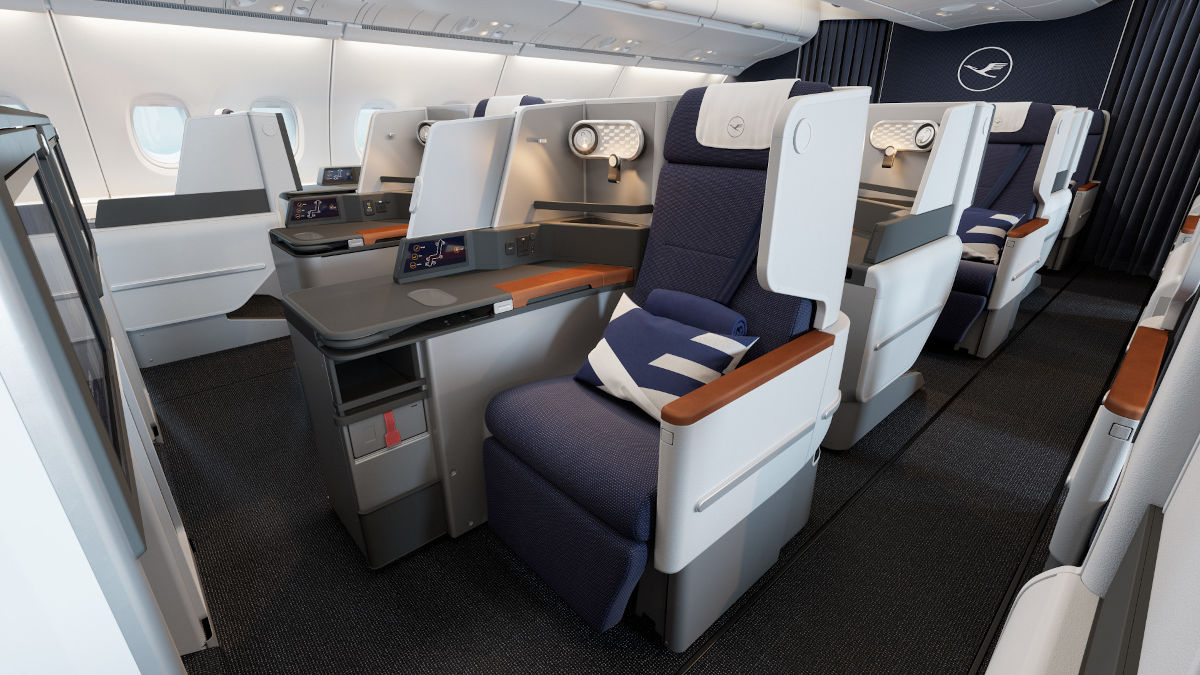 In der modernen Business Class Kabine eines Lufthansa-Flugzeugs sind komfortable Sitze mit großzügigem Platzangebot, hochwertigen Materialien und individueller Beleuchtung zu sehen. Die Sitze sind mit blauen Kissen und Decken ausgestattet und bieten viel Privatsphäre für entspanntes Fliegen. Das Bild zeigt das luxuriöse Ambiente und den gehobenen Komfort der Lufthansa Business Class.