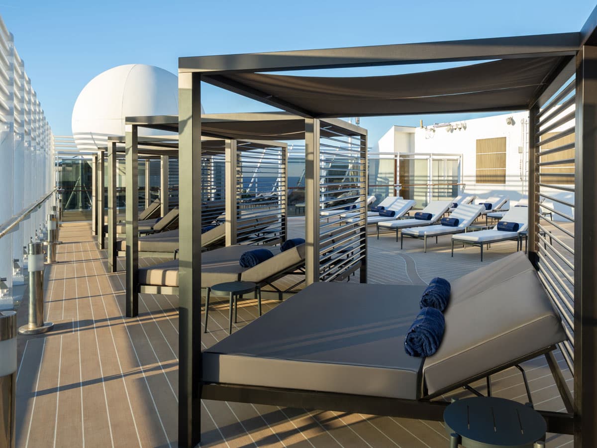 Auf dem Bild ist das private Sonnendeck des MSC Yacht Club mit komfortablen Cabanas, Liegestühlen und farblich abgestimmten Handtüchern bei schönem Wetter zu sehen. Die stilvolle Einrichtung und das offene Deck vermitteln ein Gefühl von exklusivem Luxus auf einer Kreuzfahrt.