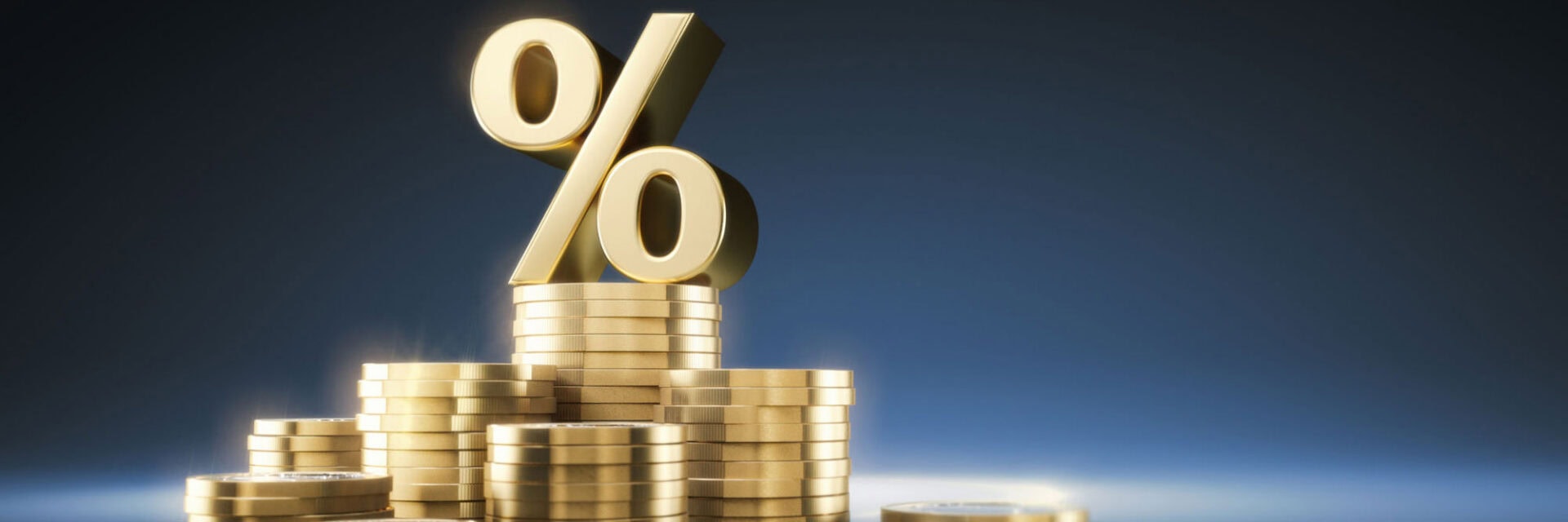 Goldenes Prozentzeichen thront auf gestapelten Goldmünzen vor dunkelblauem Hintergrund und symbolisiert Zinsen, Rendite sowie finanzielles Wachstum beziehungsweise Umsatzrückgang.