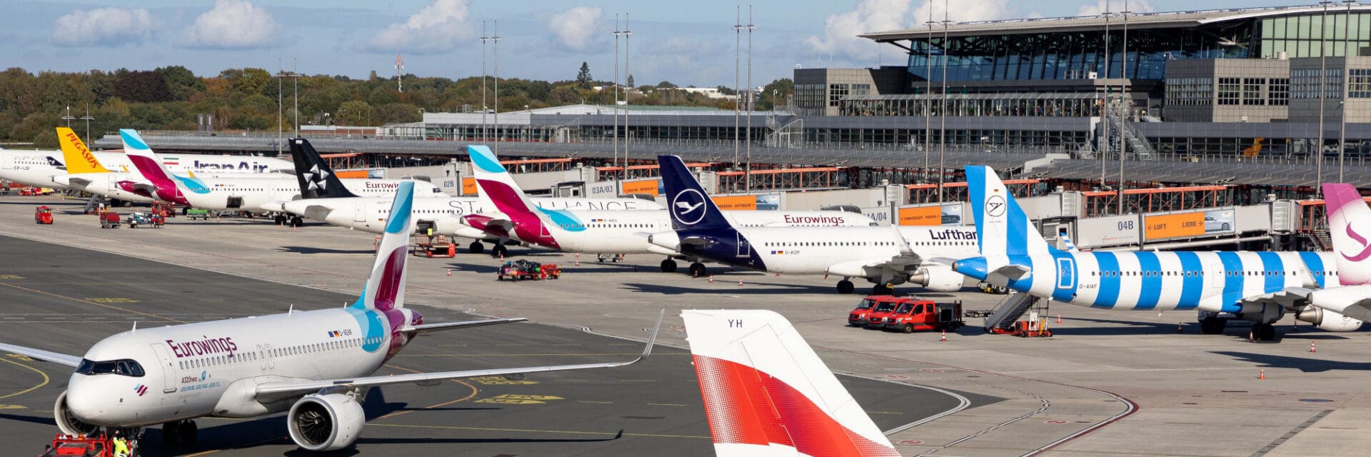 Mehrere Flugzeuge verschiedener Airlines stehen am Flughafen Hamburg auf dem Vorfeld, bereit für das Boarding. Im Hintergrund sind das moderne Terminalgebäude und zahlreiche Gates zu sehen. Das Bild zeigt den internationalen Flugverkehr und die Bedeutung des Hamburger Flughafens als Drehkreuz in Norddeutschland.