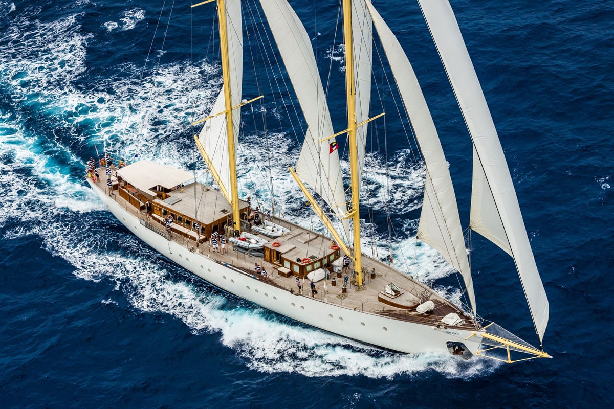 Großes weißes Segelschiff mit mehreren Masten und vollen Segeln fährt bei sonnigem Wetter durch das tiefblaue Meer, umgeben von weißen Wellen