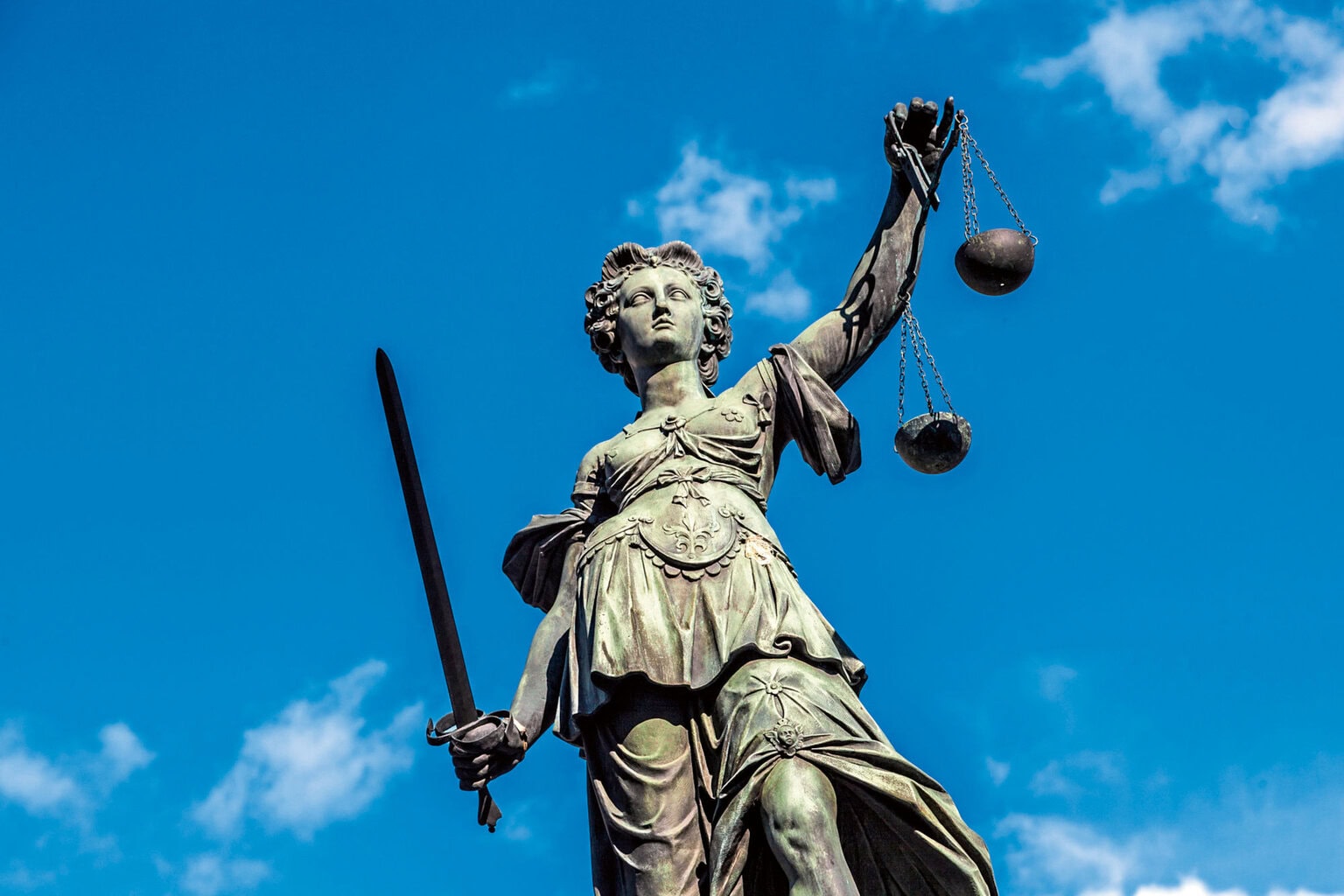 Eine Statue von Justizia vor strahlend blauem Himmel mit kleinen Schleierwolken