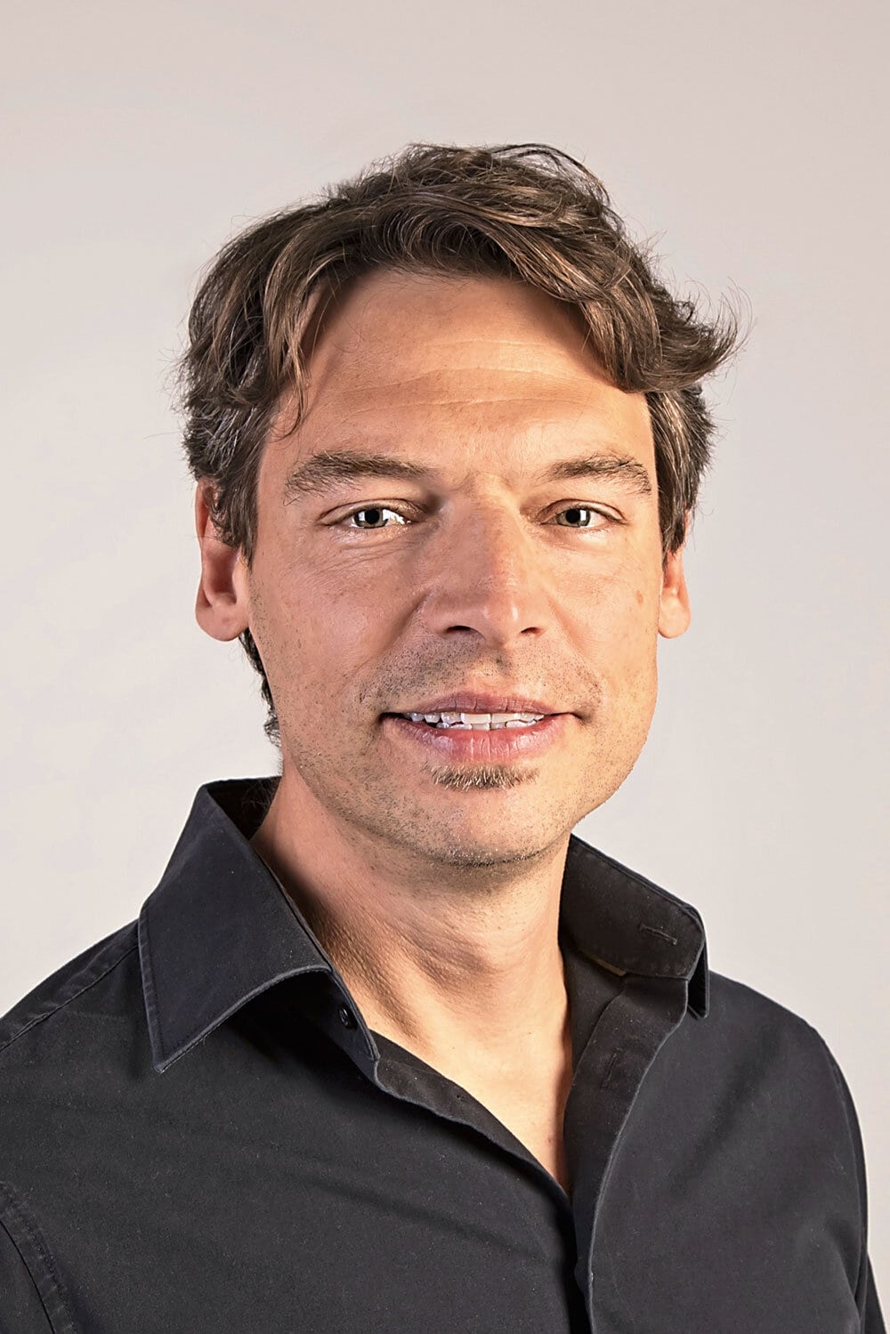 Ein Mann mit dunklem lockigen Haar und schwarzem Hemd lächelt in die Kamera