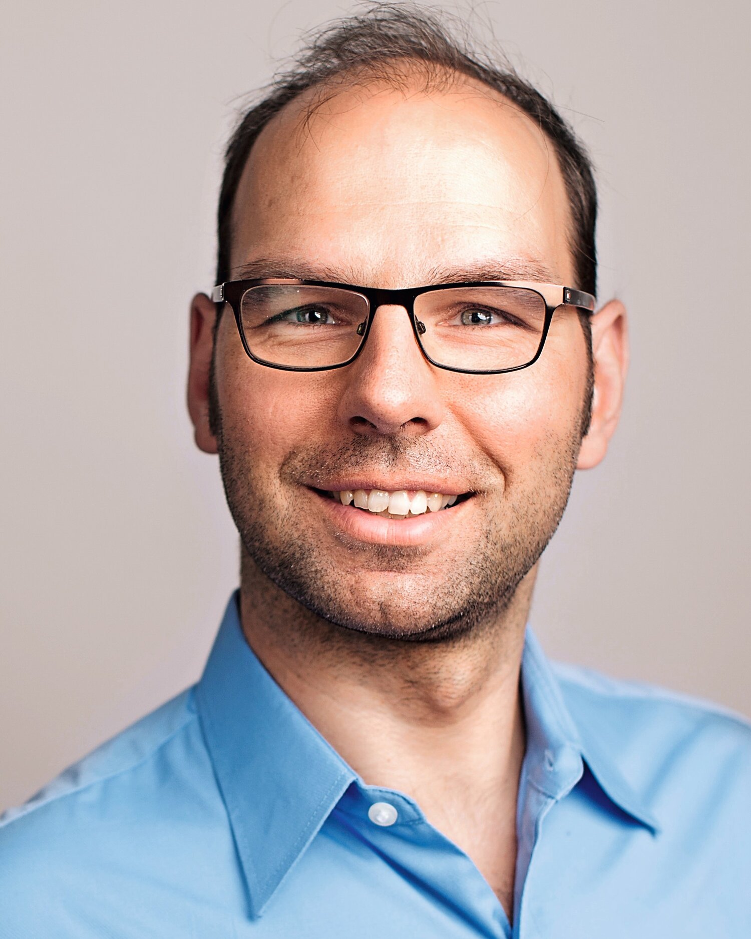 Ein Mann mit lichtem Haar, blauem Hemd und Brille lacht in die Kamera