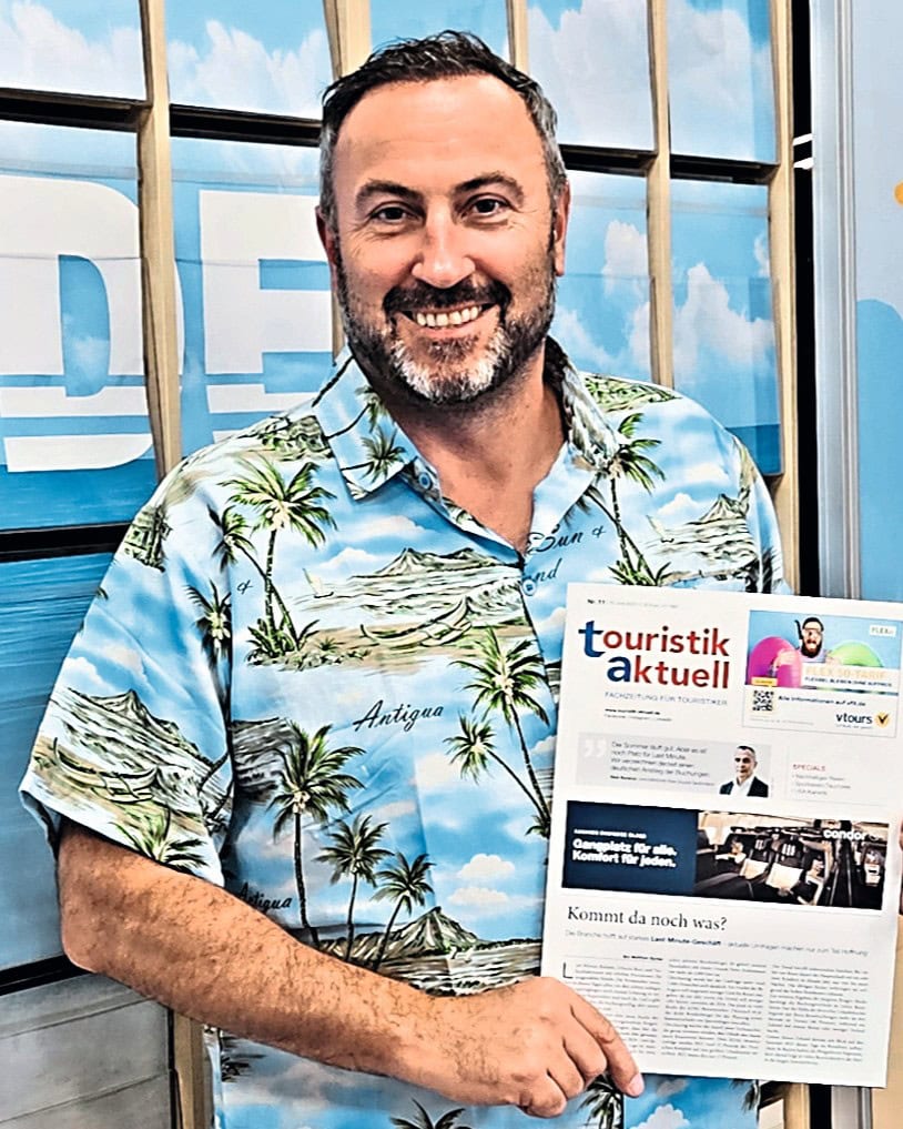 Ein Mann mit einer Ausgabe von touristik aktuell in der Hand und Hawai-Hemd lacht in die Kamera