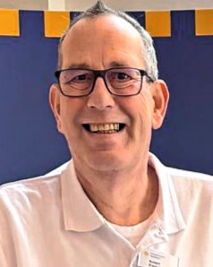 Ein Mann mit dunkler Brille, weißem Hemd lacht in die Kamera