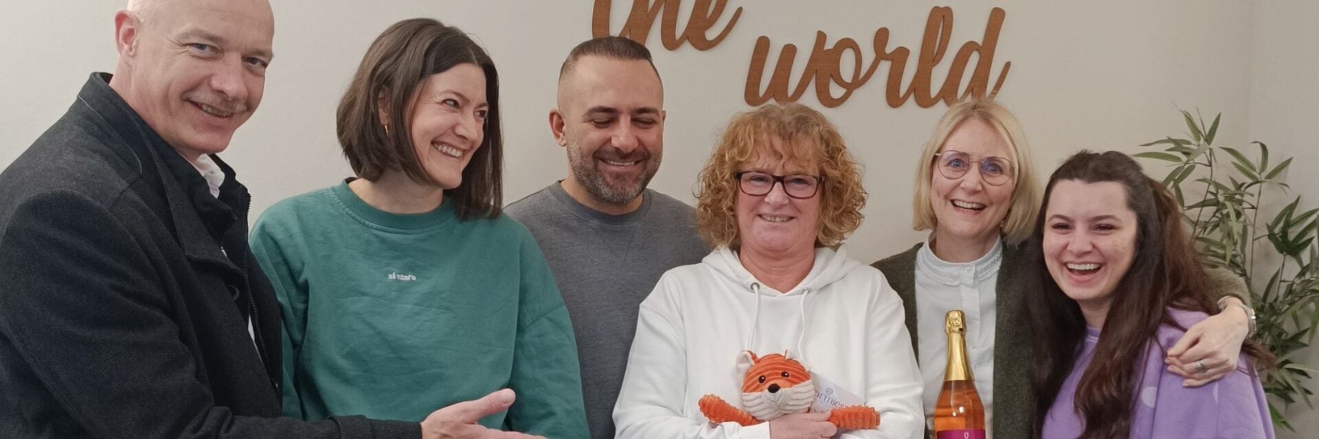 Gruppe von Gewinnern, die in die Kamera lächeln, die Frau in der Mitte hat eine Flasche Sekt in der Hand.