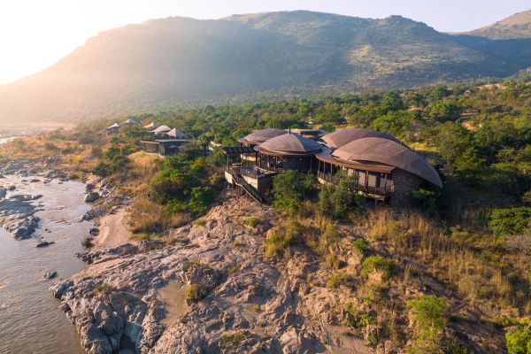 Mehrere Lodges liegen an einer Steilküste, im Hintergrund sind Berge zu sehen