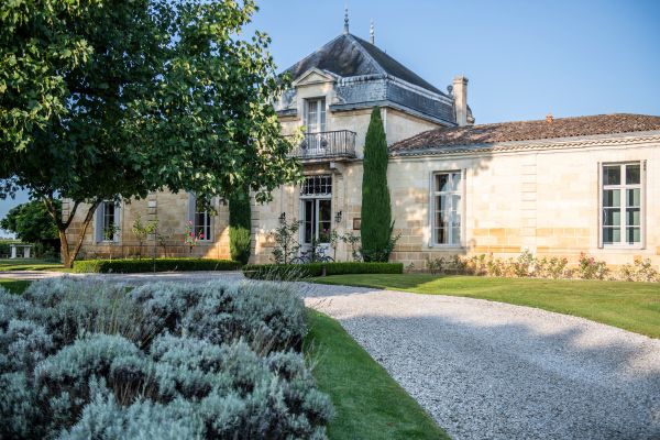 Abgebildet ist eine prachtvolle Villa im französischen Stil mit hellen Steinmauern, hohen Fenstern, einem gepflegten Vorgarten und einem geschwungenen Kiesweg.