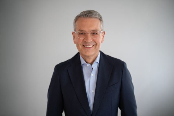 Ein Mnnn mit kurzen grauen Haaren und Brille im Anzug lächelt in die Kamera