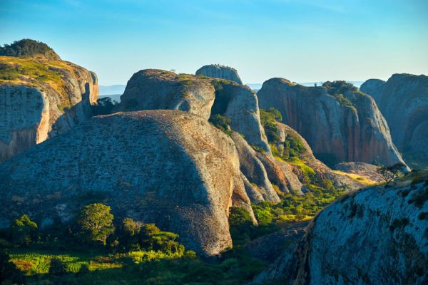 Die Fotografie zeigt die beeindruckenden Pedras Negras in Angola, eine markante Felsformation mit sanft abgerundeten Granitblöcken, umgeben von üppigem Grün und strahlendem Sonnenlicht. Die Landschaft wirkt majestätisch und unberührt.