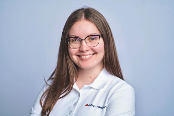 Eine junge Frau mit langen braunen Haaren und Brille lächelt in die Kamera