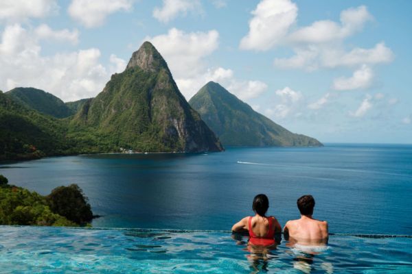 Zwei Menschen genießen den Ausblick von einem Infinity-Pool auf die berühmten Pitons auf Saint Lucia, umgeben von türkisblauem Meer und tropischer Natur.