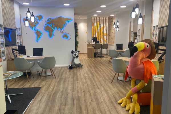 Innenansicht eines hellen, modern eingerichteten Reisebüros mit Beratungstischen, Weltkarten-Wand, Holzfußboden und dekorativen Reiseelementen.