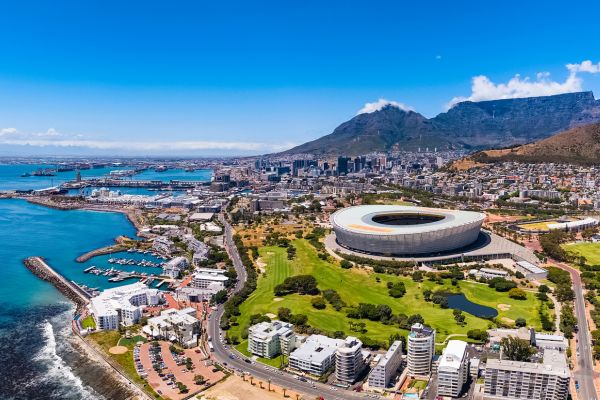 Blick auf eine Stadt mit großem Stadion. Die Stadt liegt am Meer, im Hintergrund ist ein Berg zu sehen