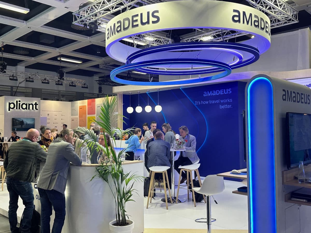 Auf dem Foto ist der moderne Messestand von Amadeus auf der ITB-Messe zu sehen, an dem mehrere Personen in Gespräche vertieft sind. Die auffällige LED-Beleuchtung und das große Amadeus-Logo betonen die innovative Technologie im Bereich Reise- und Tourismusbranche.