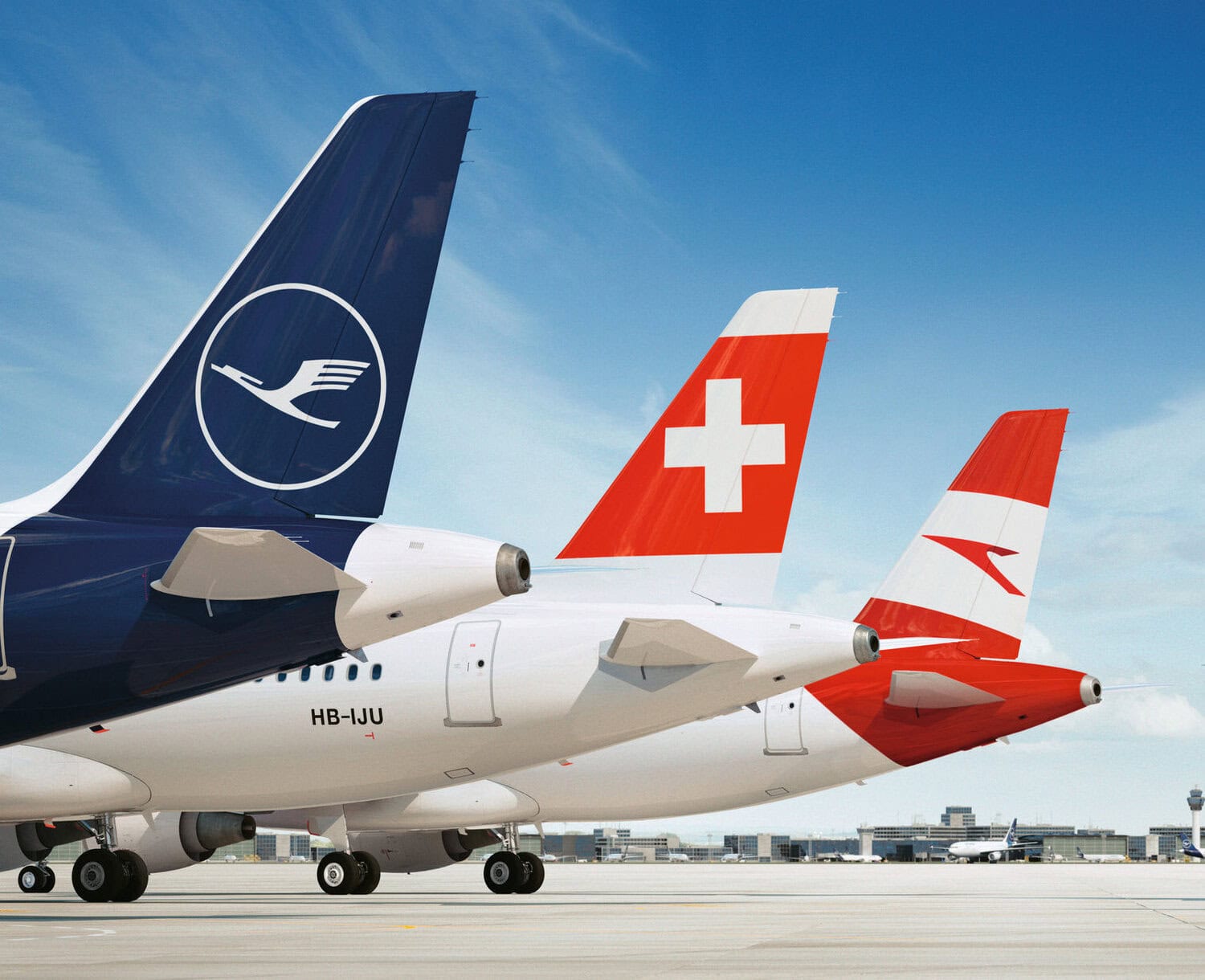 Drei Flugzeuge der Airlines Lufthansa, Swiss und Austrian stehen nebeneinander auf dem Rollfeld eines Flughafens, ihre markanten Leitwerke mit den Firmenlogos sind deutlich sichtbar; das Bild illustriert die Vielfalt europäischer Fluggesellschaften und den internationalen Flugverkehr.
