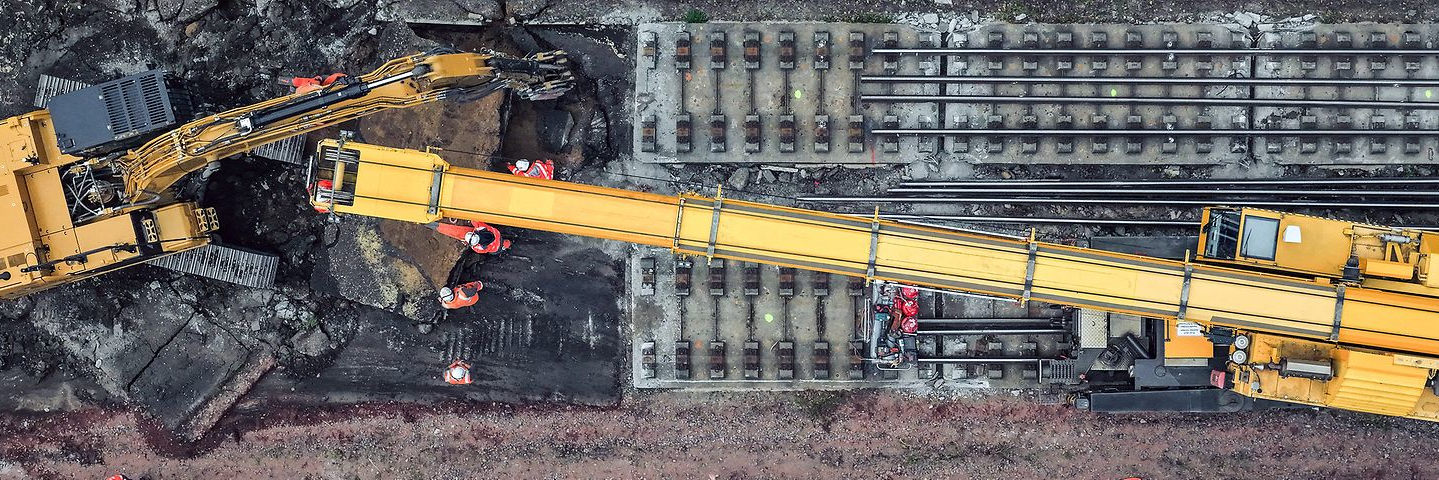 Luftaufnahme einer Baustelle an Bahngleisen: Zwei große Baufahrzeuge und mehrere Bauarbeiter in Warnwesten erneuern eine Bahnstrecke zwischen Hamburg und Berlin, um die Infrastruktur der Deutschen Bahn zu modernisieren.