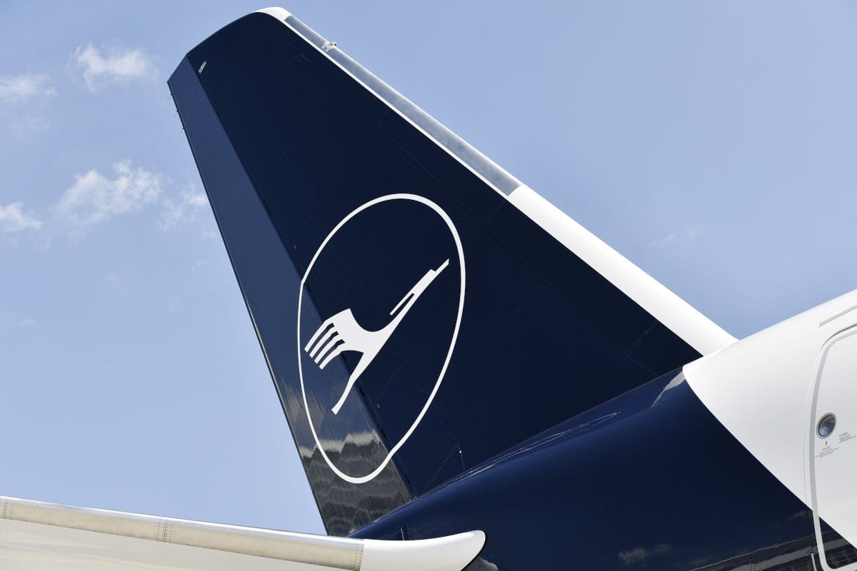 Das Foto zeigt das Seitenleitwerk eines Lufthansa-Flugzeugs mit dem bekannten Kranich-Logo auf dunkelblauem Hintergrund vor klarem Himmel. Das Bild hebt das moderne Design und die Markenidentität der Lufthansa hervor.