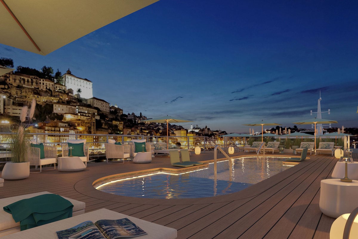 Das Foto zeigt das stilvolle Pooldeck eines Flusskreuzfahrtschiffs bei Nacht vor der beleuchteten Altstadt von Porto; im Vordergrund sind Liegen und Sitzgelegenheiten, im Hintergrund die berühmten historischen Gebäude Portos.