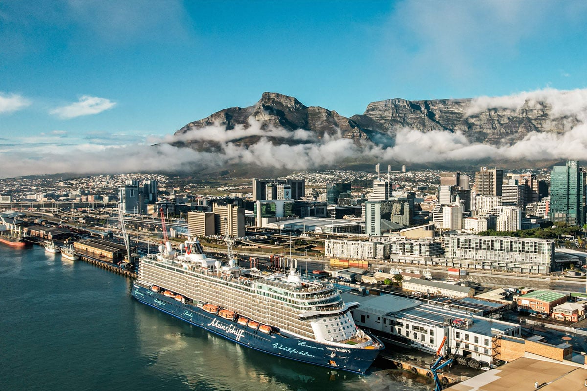 Vor den Kulisse von Kapstadt liegt ein Kreuzfahrtschiff von TUI Cruises. Die Sonne scheint.
