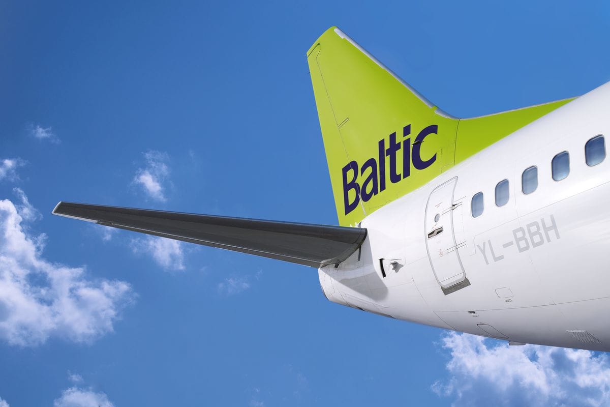 Das Foto zeigt das auffällig grüne Leitwerk eines Flugzeugs der Fluggesellschaft Air Baltic vor blauem Himmel mit weißen Wolken. Deutlich ist das Branding „Baltic“ auf dem Seitenleitwerk erkennbar, was auf die lettische Airline hinweist.