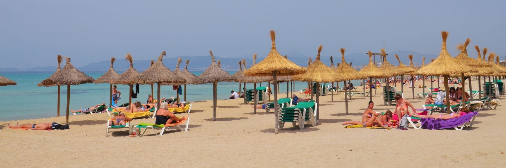 Ansicht von Strand in Mallorca mit Sonnenschirmen, Liegen und badenden Touristen