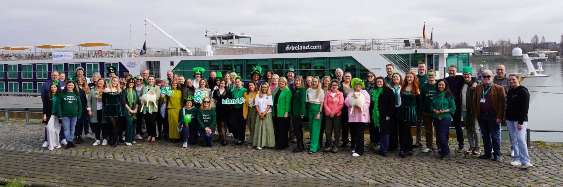 Gruppenfoto von Teilnehmern der irischen Floating Roadshow vor einem Flusskreuzfahrtschiff am Rhein, viele in grüner Kleidung zum St. Patrick’s Day.