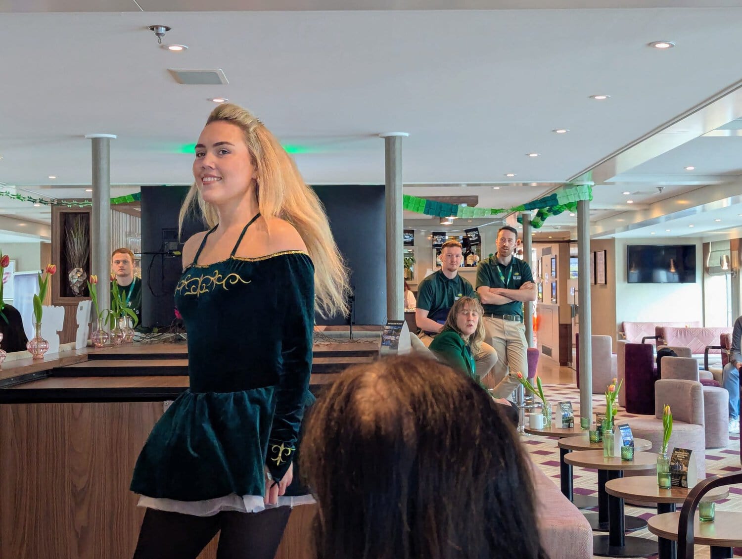Irish-Dance-Tänzerin in traditionellem Kostüm bei einer Aufführung an Bord eines Flusskreuzfahrtschiffs, Zuschauer im Hintergrund.