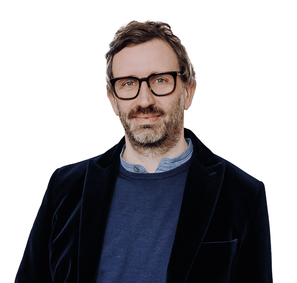 hieke-ralf-1000x953px Ein Mann mit einem dunklen Sakko und dunkler Brille lächelt in die Kamera