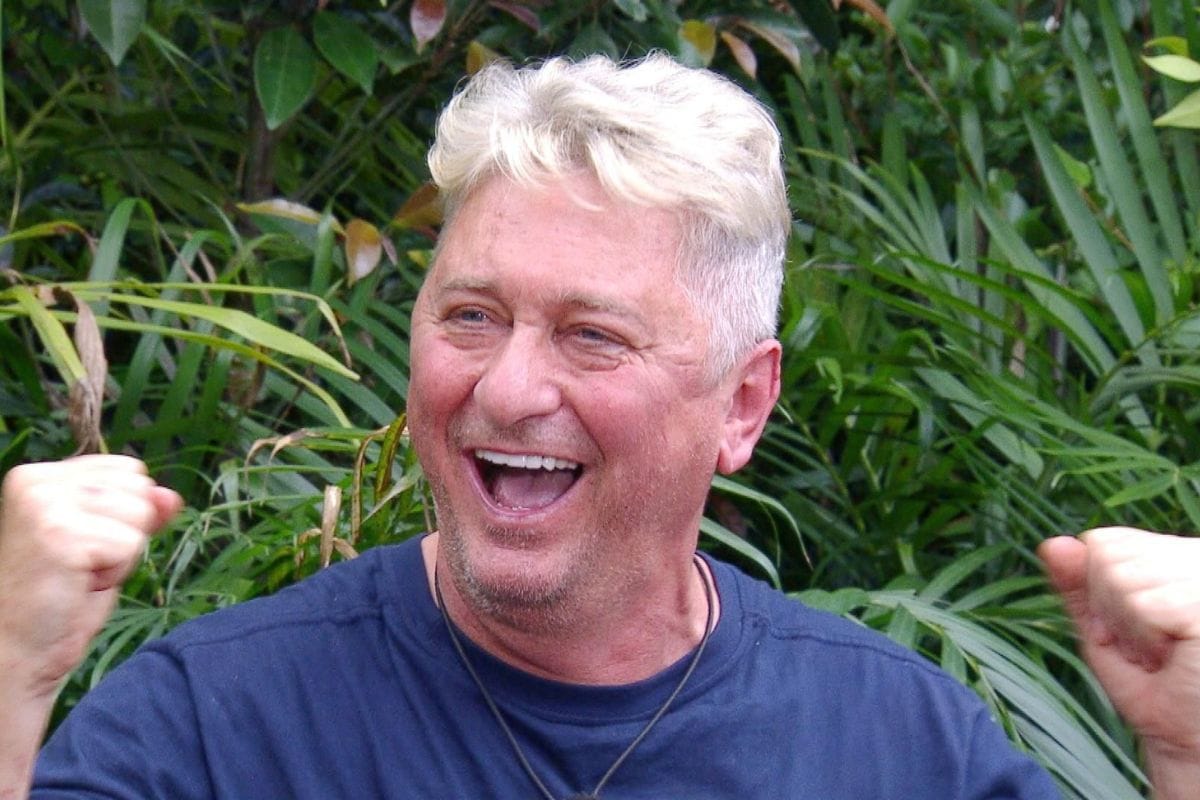 Hubert Fella im Dschungelcamp jubelnd mit erhobenen Fäusten vor grüner Dschungelkulisse.