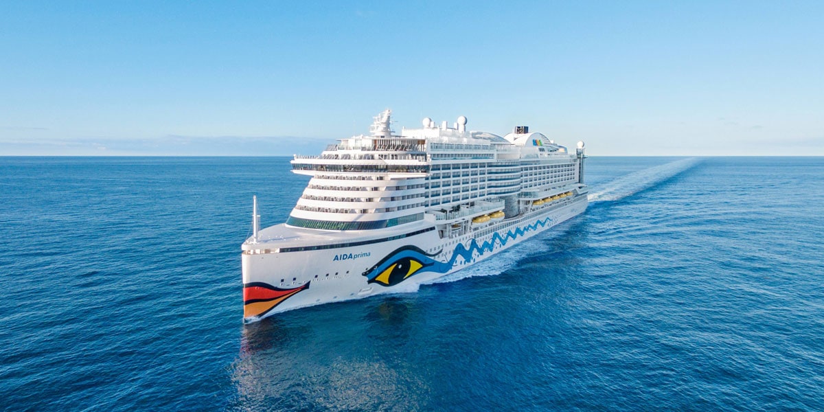 Das Kreuzfahrtschiff Aida Prima unterwegs auf hoher See. Die Sonne scheint auf das blaue Meer.