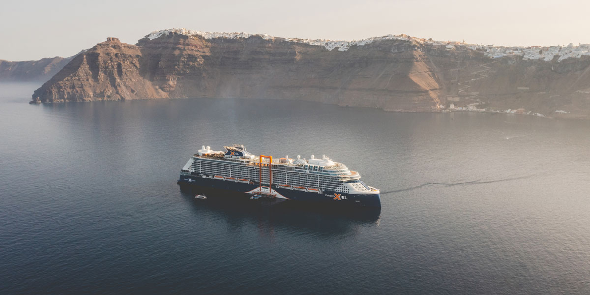 Luftaufnahme von einem modernen Kreuzfahrtschiff mit blauem Rumpf vor Santorin.
